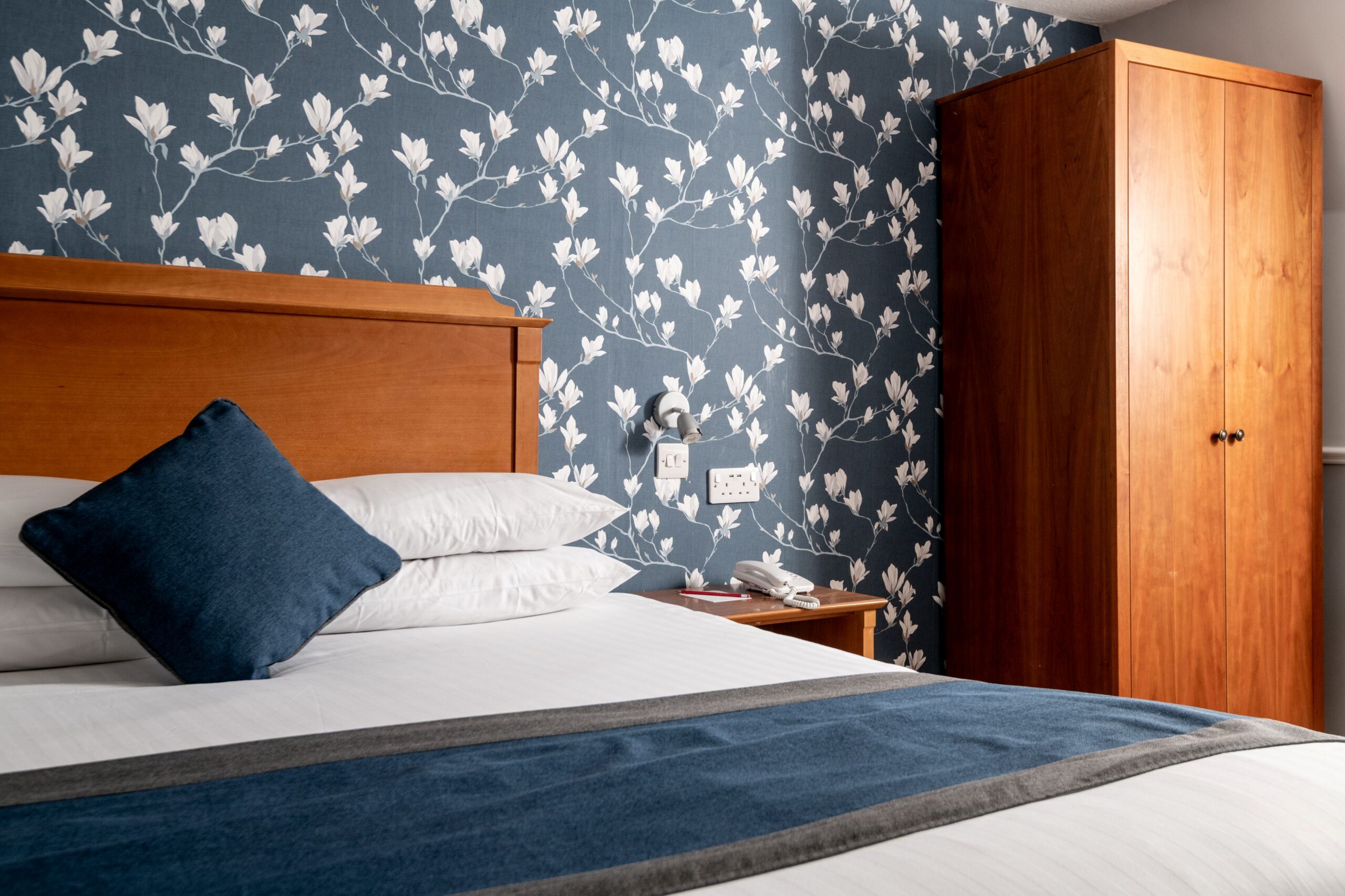 Double bed with blue cushions and a patterned feature wall