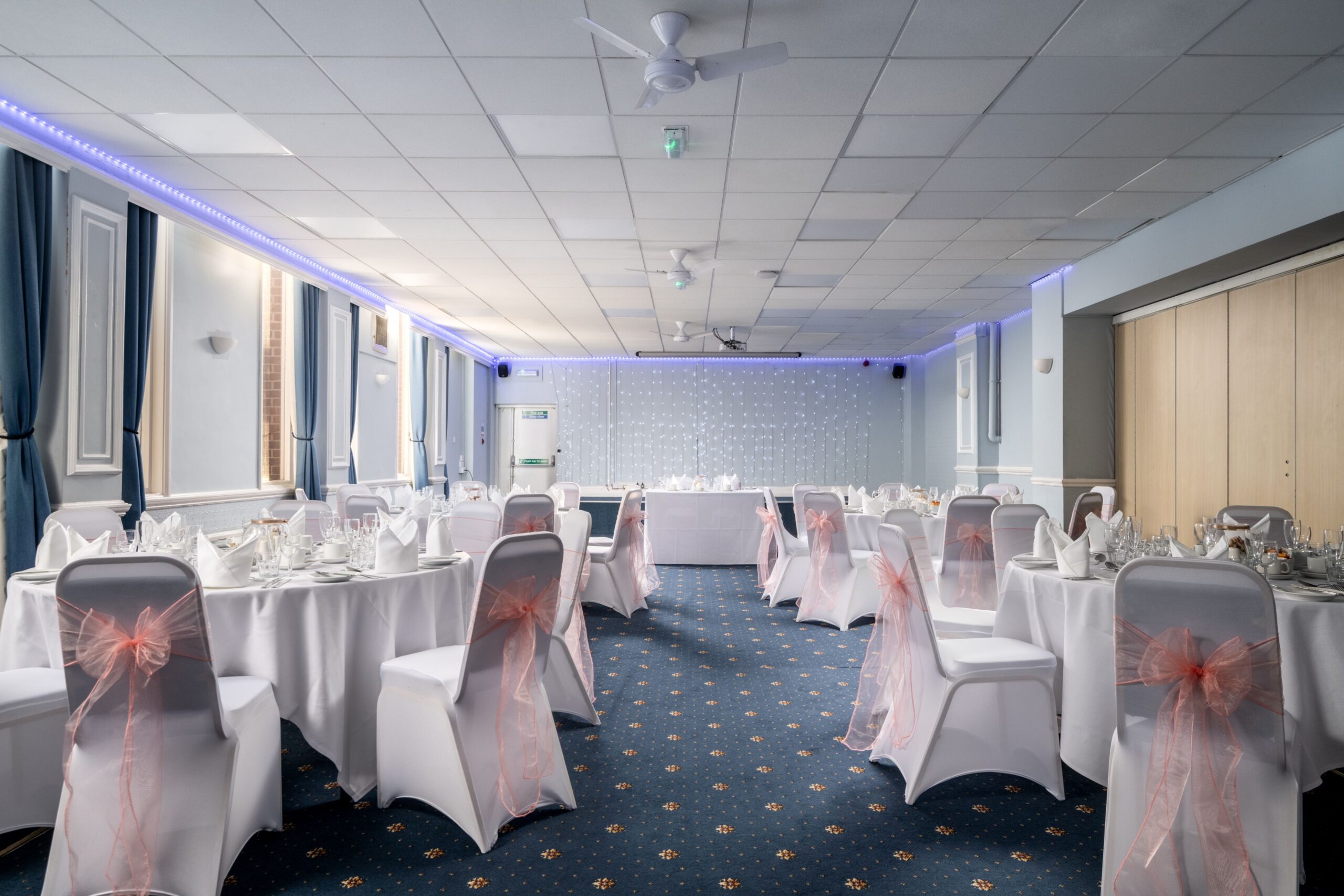 Wedding reception tables with white chair covers and pink sashes